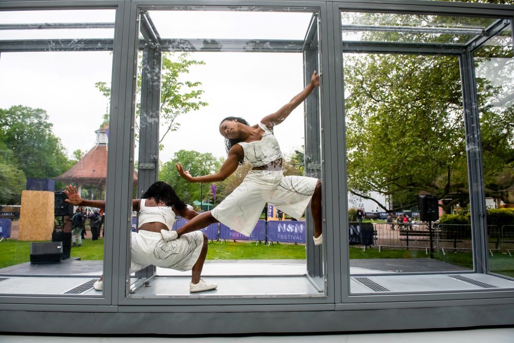 two dancers doing acrobatics inside perspex glass box