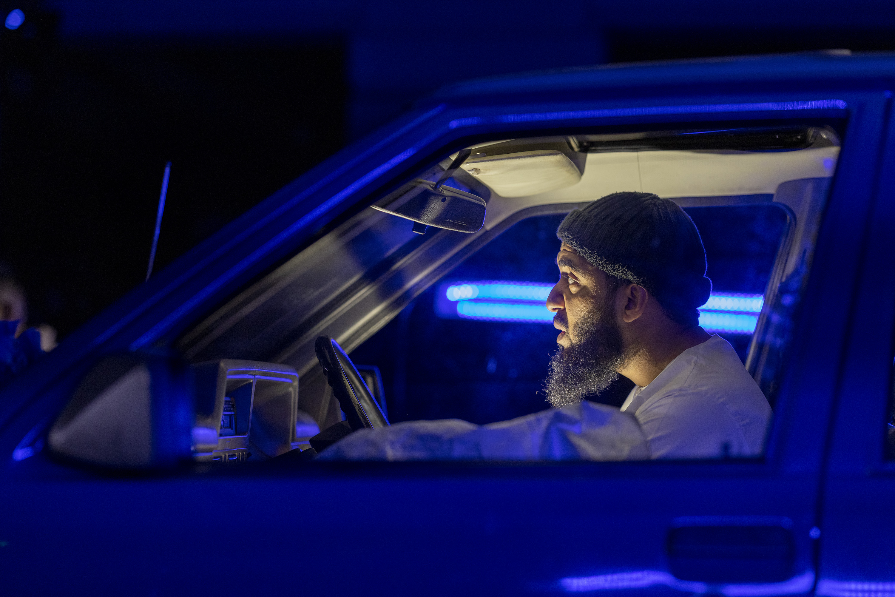 dramatically lit shot of a Muslim Pakistani man at the wheel of his modified car