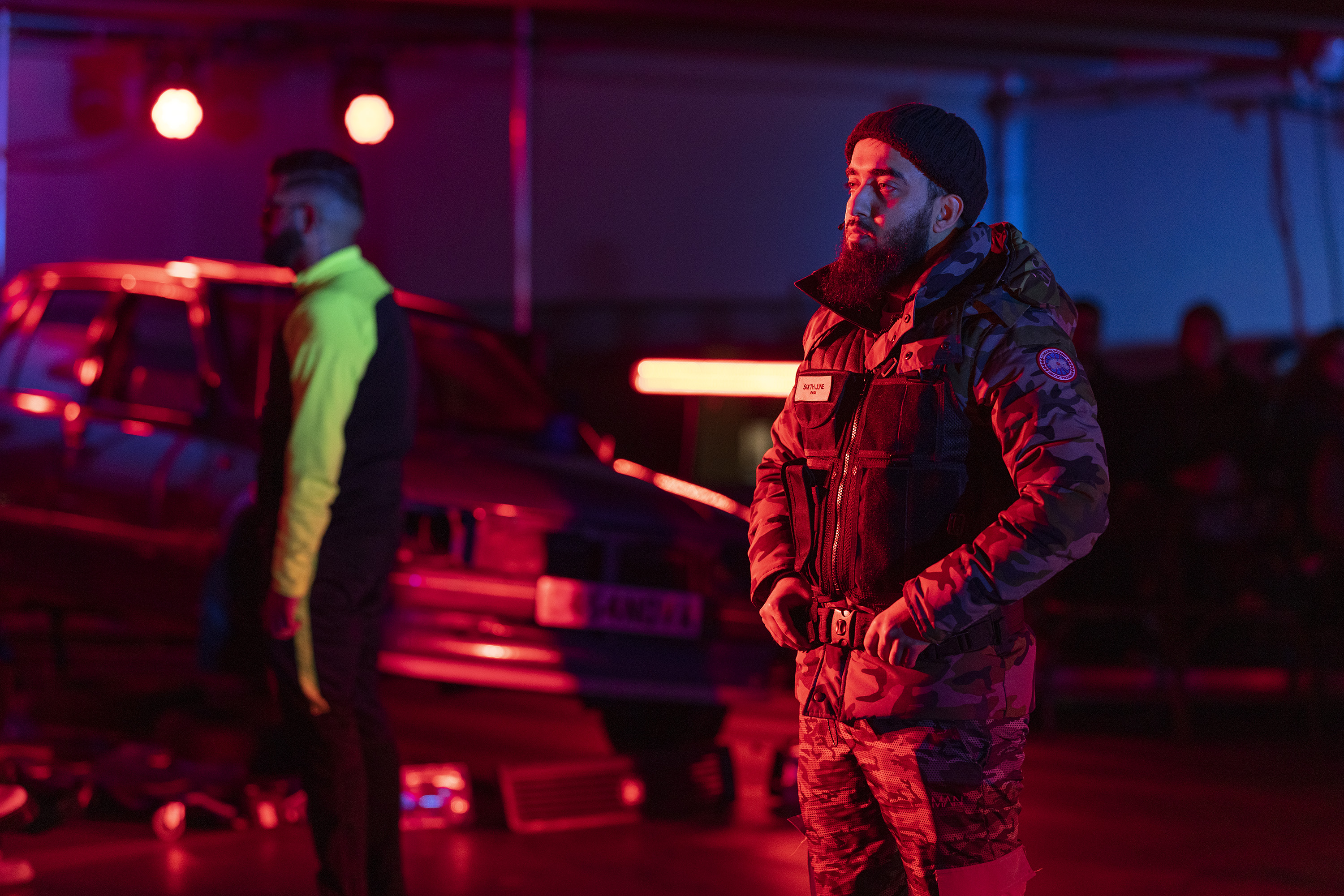 a man in camo gear stands in front of a dramatically lit modified car