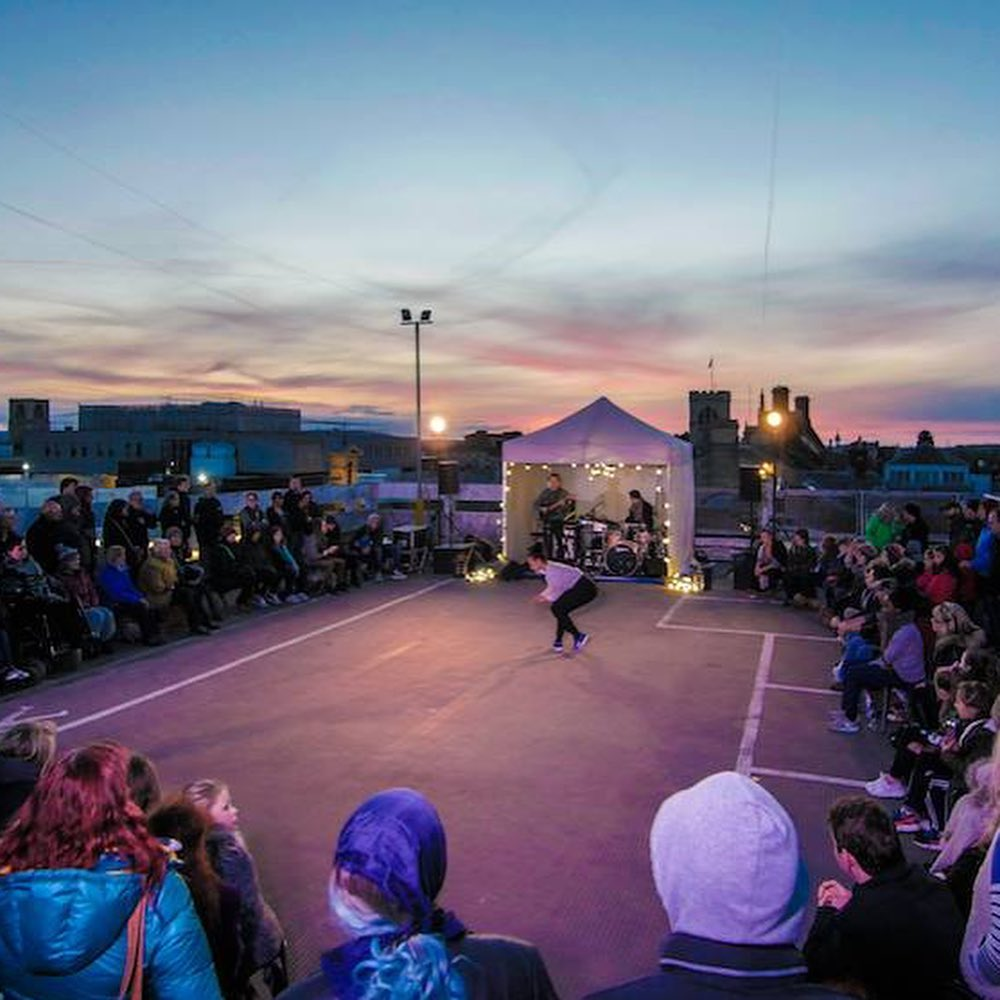 a dancer performs a routine in the middle of a watching audience on top of a car park at night